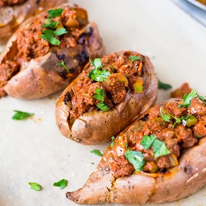 Sloppy joe stuffed sweet potatoes on parchement paper on top of baking sheet